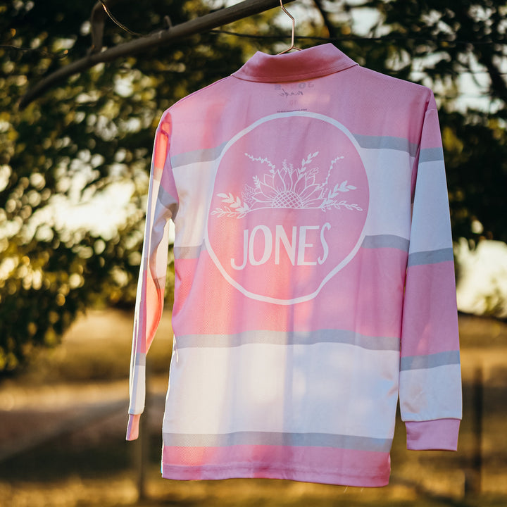 A pink and white striped long-sleeve athletic jersey with a circular 'JONES' logo on the back, hanging from a tree branch outdoors.