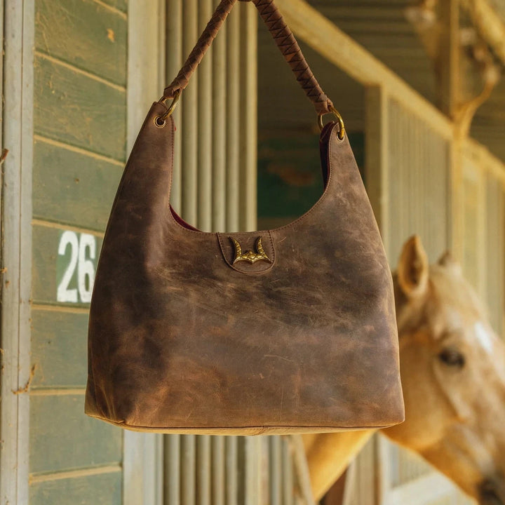 Brown leather handbag hanging on a hook with a horse in the background