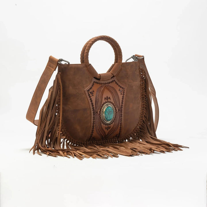 A brown leather fringe handbag with a circular top handle, a turquoise stone inlay on the front, and a long adjustable shoulder strap, photographed against a plain white background.