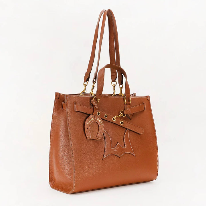 A brown leather tote bag with gold-tone hardware, featuring a decorative horsebit charm and a horse silhouette patch on the front, set against a plain white background.
