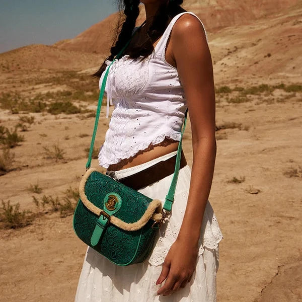 Woman in a white outfit and cowboy hat holding a green bag in a desert setting