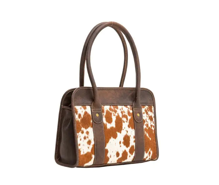 A structured handbag with dark brown leather trim and handles, featuring a front panel with vertical brown and white cowhide print panels.