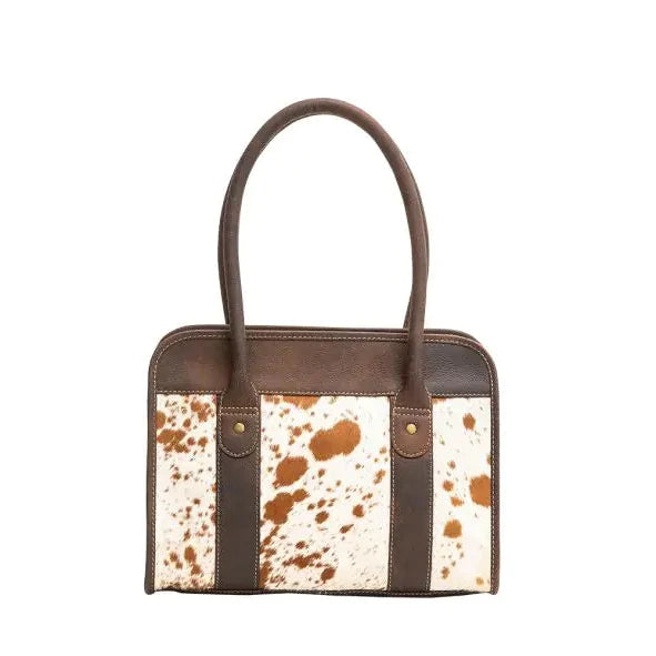 A structured handbag with dark brown leather handles and trim, featuring a front panel with a white and brown cowhide pattern.